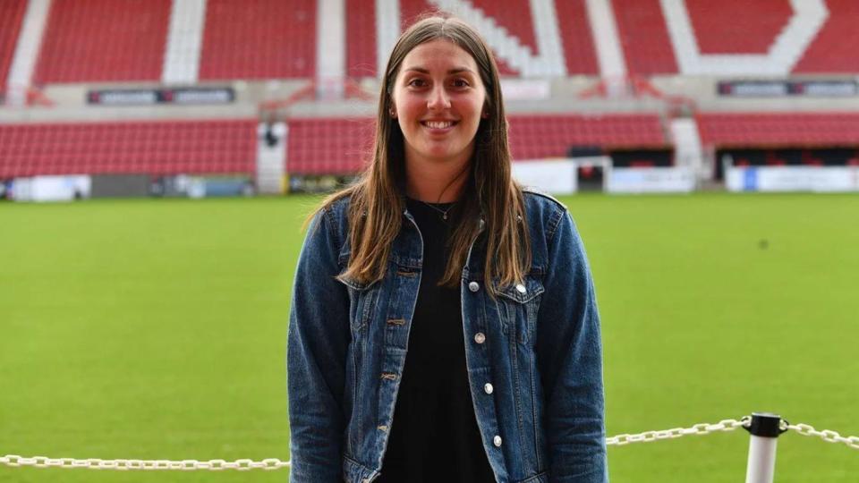 Vicki Eyles in a denim jacket in front of Swindon Town football pitch