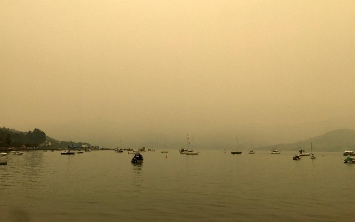 A yellow light illuminates the sky as the sun sets over Akaroa Harbor as smoke from the Australian wildfires arrives on the east coast of the South Island, New Zealand - AP