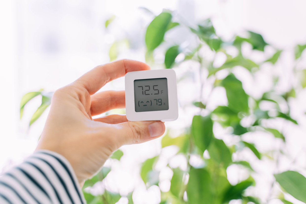 person holding temperature and humidity monitor to show indoor temperature and humidity levels inside the home