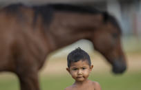 A young member of the Macuxi ethnic group stand near a horse in the Maturuca community of the Raposa Serra do Sol Indigenous reserve in Roraima state, Brazil, Sunday, Nov. 7, 2021. Bordering Venezuela and Guyana, the Indigenous territory is bigger than Connecticut and home to 26,000 people from five different ethnicities. (AP Photo/Andre Penner)