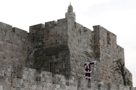 Israeli-Arab Issa Kassissieh wears a Santa Claus costume as he stands on Jerusalem's Old City walls during the annual Christmas tree distribution by the Jerusalem municipality in Jerusalem's Old City December 21, 2017. REUTERS/Ammar Awad