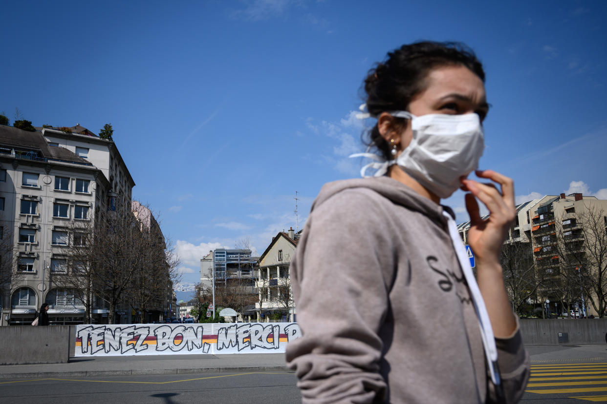 A woman wearing a protective face mask walks by a giant banner reading : "Hold on, thank you for everything" deployed in front of the Geneva University Hospitals (HUG) as a lockdown is in effect to prevent the spread of the COVID-19 caused by the novel coronavirus, in Geneva on March 20, 2020. (Photo by FABRICE COFFRINI / AFP) (Photo by FABRICE COFFRINI/AFP via Getty Images)