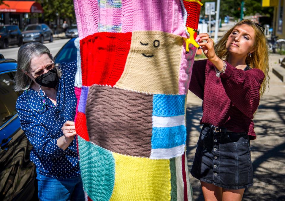Indiana University sophomore Macee Long, right, and Mary Lostutter work on knitting a sweater on a tree on the northeast corner of 6th Street and College Avenue for the Wrapped in Love event benefitting Bloomington's Middle Way House on Friday, September 24, 2021.