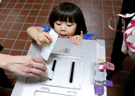 A girl casts her father's ballot for a national election at a polling station in Tokyo, Japan October 22, 2017. EUTERS/Kim Kyung-Hoon