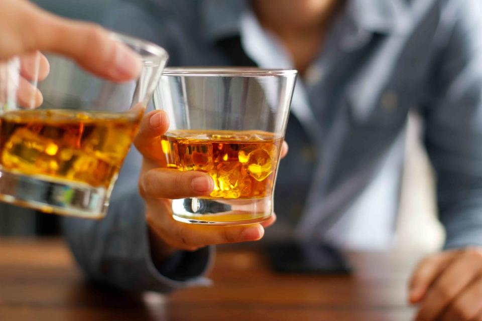 ipopba / Getty Images Close-up two men clinking glasses of an alcohol beverage