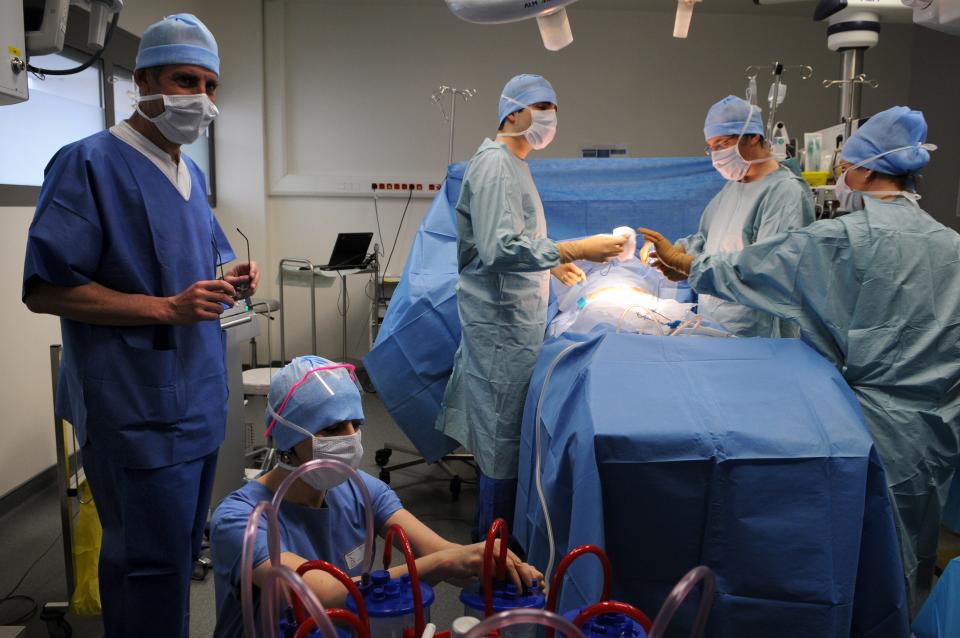 A group of nurses and surgeons stand around an operating table with a patient on it.