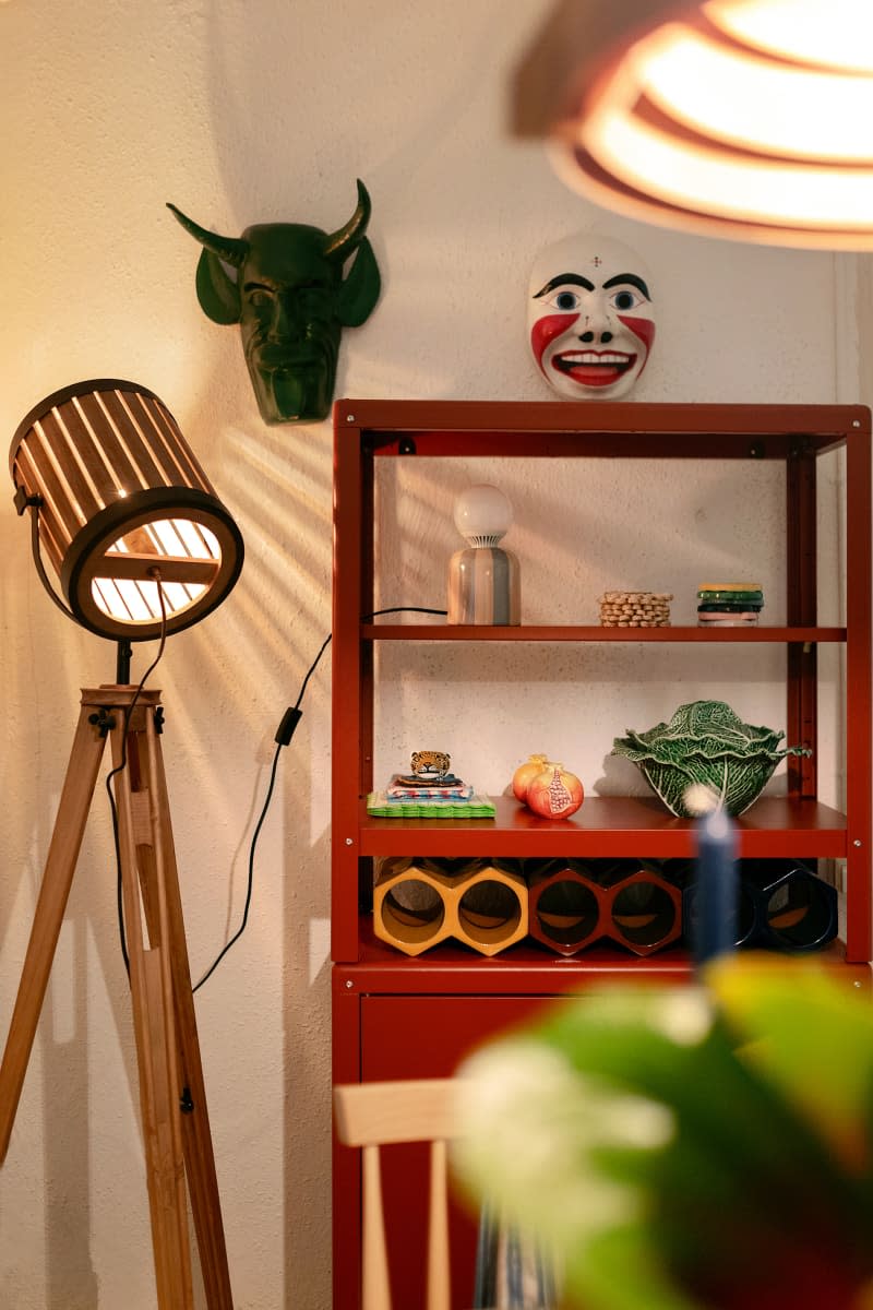 Tripod floor lamp next to red shelving unit in neutral room.