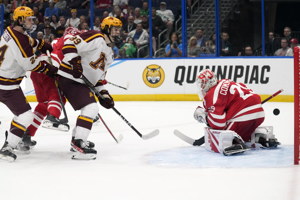 Minnesota forward Jaxon Nelson (24) and forward Matthew Knies (89) watch a shot by defenseman Mike Koster (4) get past Boston University goaltender Drew Commesso (29) for a goal during the first period of an NCAA semifinal game in the Frozen Four college hockey tournament Thursday, April 6, 2023, in Tampa, Fla. (AP Photo/Chris O'Meara)