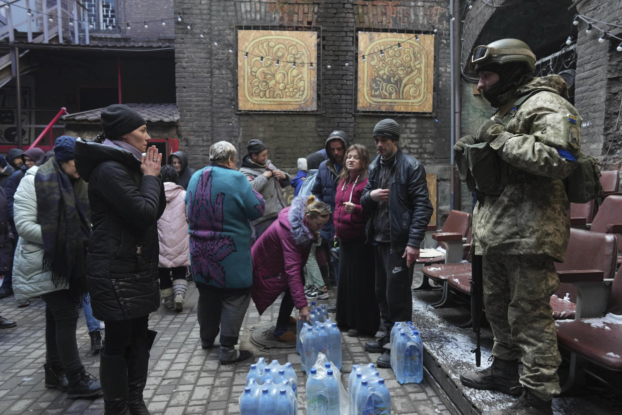 A Ukrainian servicemen distributes bottled water to people outside a building in Mariupol. 