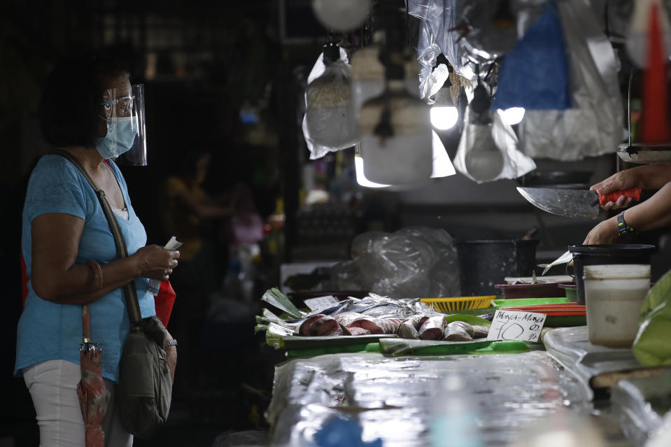 A woman wears a mask and face shield as a measure to help curb the spread of COVID19 as she buys fish at a public market on Sunday, Aug. 2, 2020, in Quezon city, Philippines. Coronavirus infections in the Philippines continues to surge Sunday as medical groups declared the country was waging a losing battle against the contagion and asked the president to reimpose a lockdown in the capital. (AP Photo/Aaron Favila)