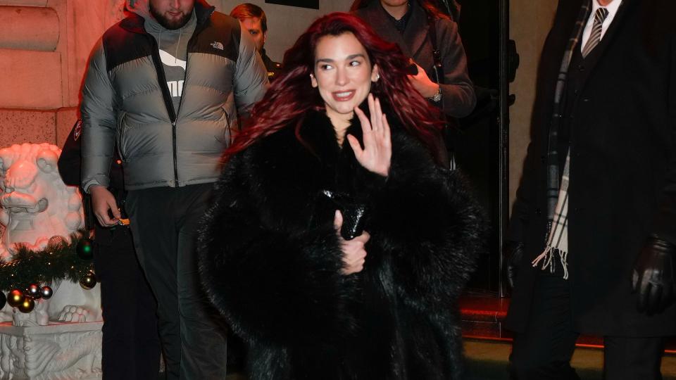 Dua Lipa wears an oversized black fur coat, lace catsuit and black knee high boots in NYC  