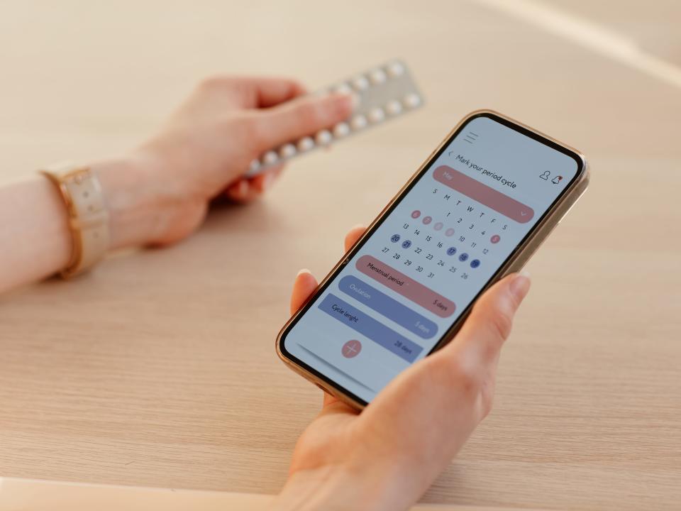 A photo of a person holding a phone with a period tracker app and a card of birth control