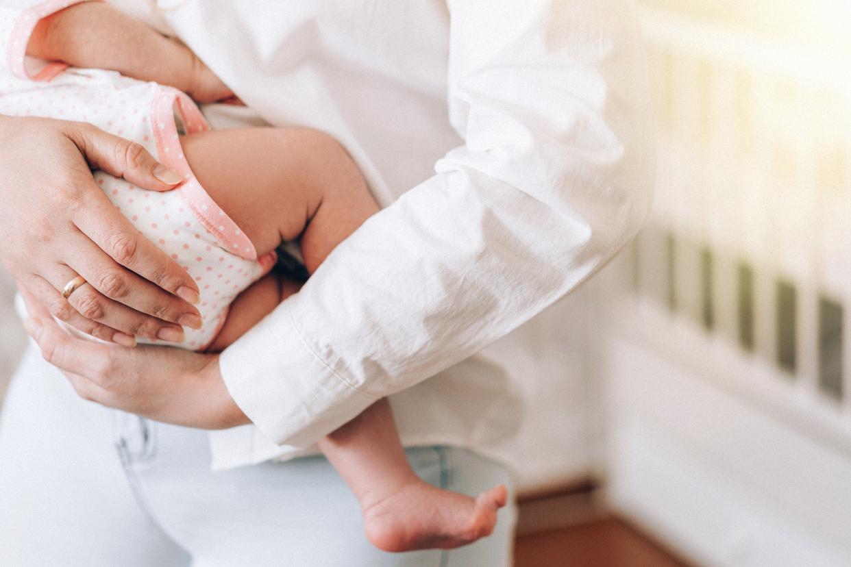 A beshirted woman's arms cradling a baby in a onesie