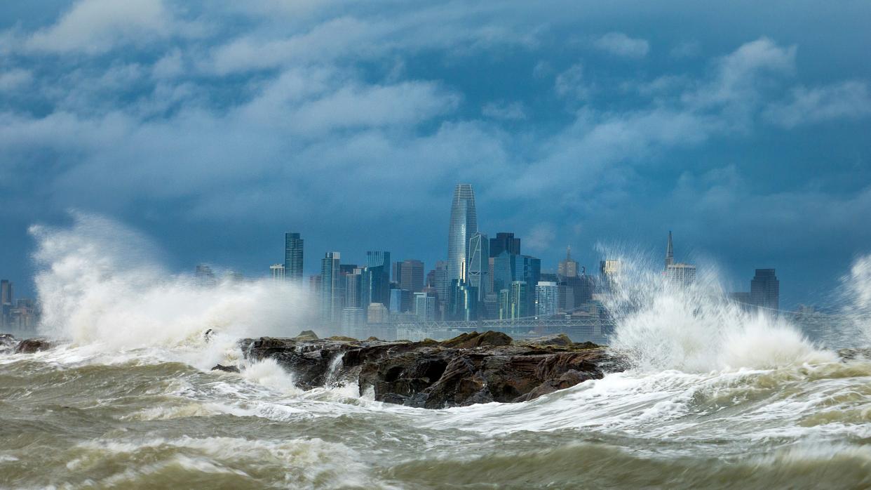 Waves crash over a breakwater in Alameda, Calif., with the San Francisco skyline in the background on Feb. 4, 2024. High winds and heavy rainfall are impacting the region.