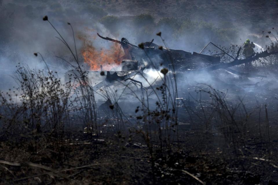 Israeli firefighters extinguish a fire burning amid grasses.