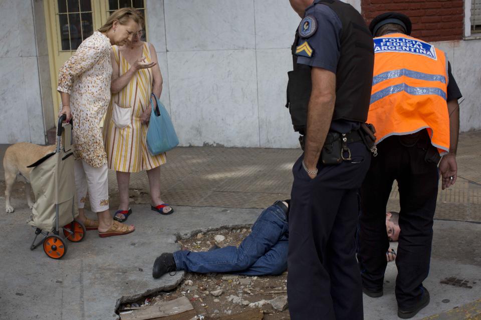 In this Jan. 24, 2014 photo, policeman stand at the side of a man they happened upon, as they wait for the arrival of an ambulance, in Buenos Aires, Argentina. Argentines have suffered through a tough summer, with tropical rain that provided no relief from the heat and humidity, people having to throw out rotten food because of rolling power blackouts and soaring oil and gas prices, all amid rising inflation that is making it ever harder to reach the end of the month. The strain is evident on the faces of subway riders and others making their way home in Buenos Aires, where signs of poverty and decay are ubiquitous just beyond the glamorous streets where tourists go. (AP Photo/Rodrigo Abd)