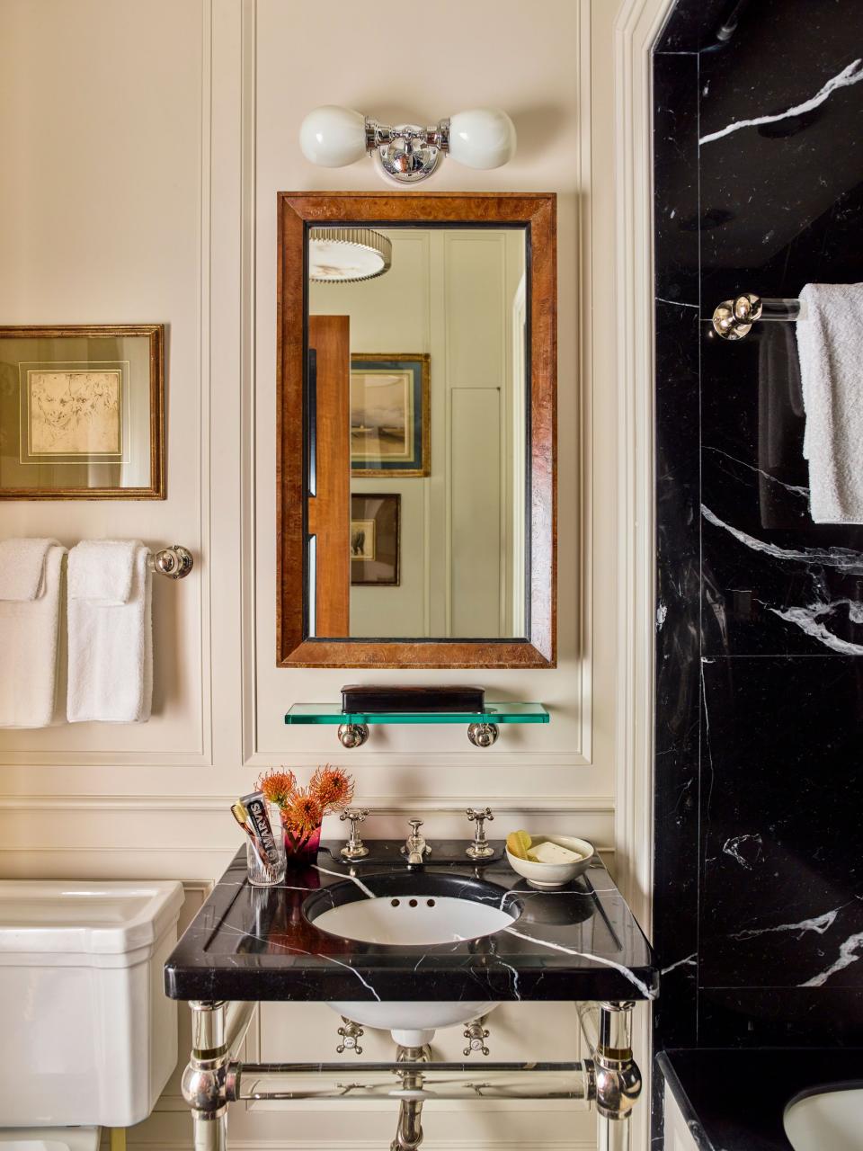 The bath echoes the apartment’s traditional aesthetic with a glass-leg sink stand from Urban Archaeology; faucets from Barber Wilsons; a custom mirror designed by Schafer; and a toilet, tub, and sconce by Waterworks. The tub enclosure and sink countertop add contrast to wood paneling in Benjamin Moore’s Seapearl thanks to Nero Marquina marble.