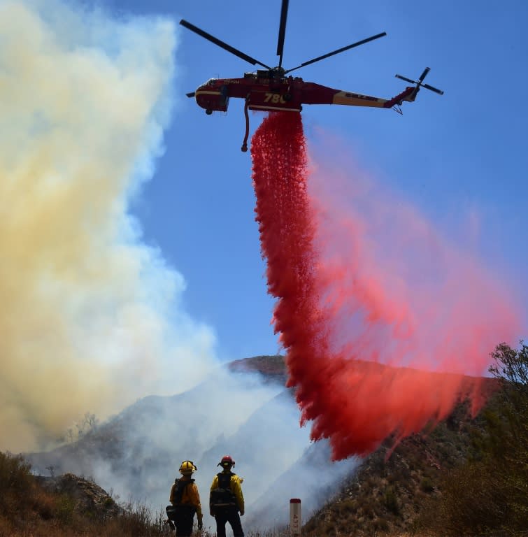 Firemen watch as a helicopter drops retardant on a fire off Placerita Canyon Road in Santa Clarita, California on July 25, 2016