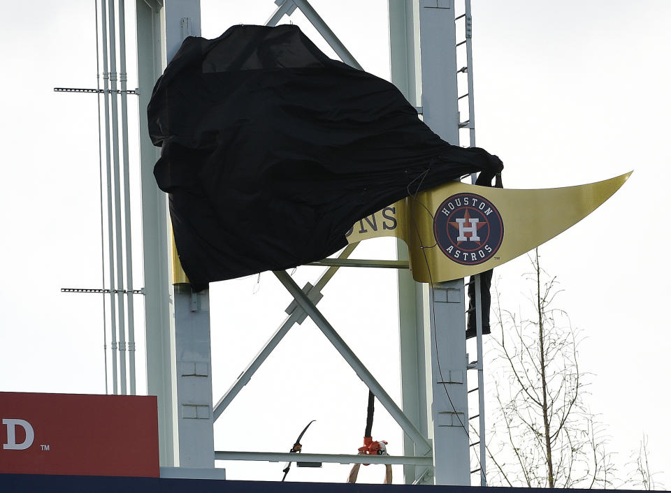 Workers try to remove the cover of the Houston Astros’ 2018 World Series champion banner before a baseball game against the Baltimore Orioles. (AP Photo/Eric Christian Smith)