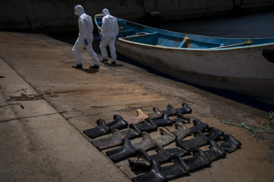 Waterproof boots are placed on the ground by police officers as they inspect a boat where 15 Malians were found dead adrift in the Atlantic on Thursday, Aug. 20, 2020 in Gran Canaria island, Spain. (AP Photo/Emilio Morenatti)