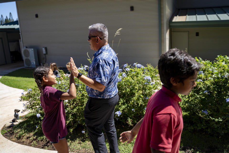 Maui Preparatory Academy head Dr. Miguel Solis high-fives a student on Tuesday, Oct. 3, 2023, in Lahaina, Hawaii. At one point the academy had taken in about 150 public school students. The three public schools that survived the deadly August wildfire are set to reopen this week. (AP Photo/Mengshin Lin)