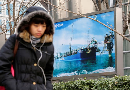 A woman walks past a China National Offshore Oil Corp (CNOOC) poster showing an offshore work platform, next to its headquarters in Beijing, December 10, 2012. REUTERS/Jason Lee/File Photo