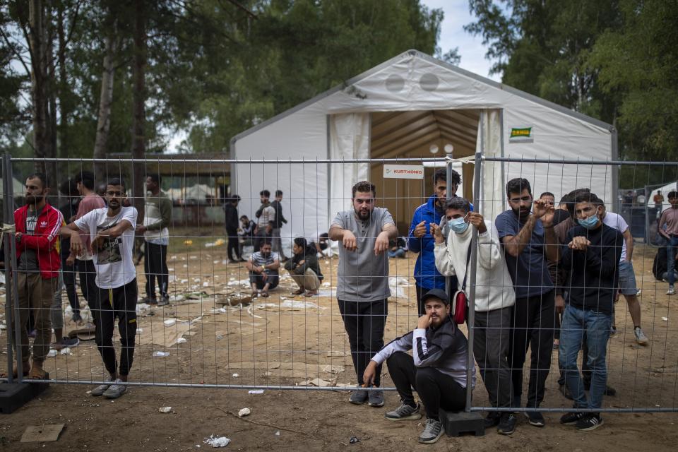 FILE - In this file photo taken on Wednesday, Aug. 4, 2021, Migrants stand by the fence at the at the newly built refugee camp in the Rudninkai military training ground, some 38km (23,6 miles) south from Vilnius, Lithuania. Lithuanian authorities said Friday that the Baltic country has stemmed the flow of third country migrants illegally crossing from neighboring Belarus, saying the influx of people knocking at the external border of European Union seems to have halted and hundreds have been turned away.(AP Photo/Mindaugas Kulbis, File)