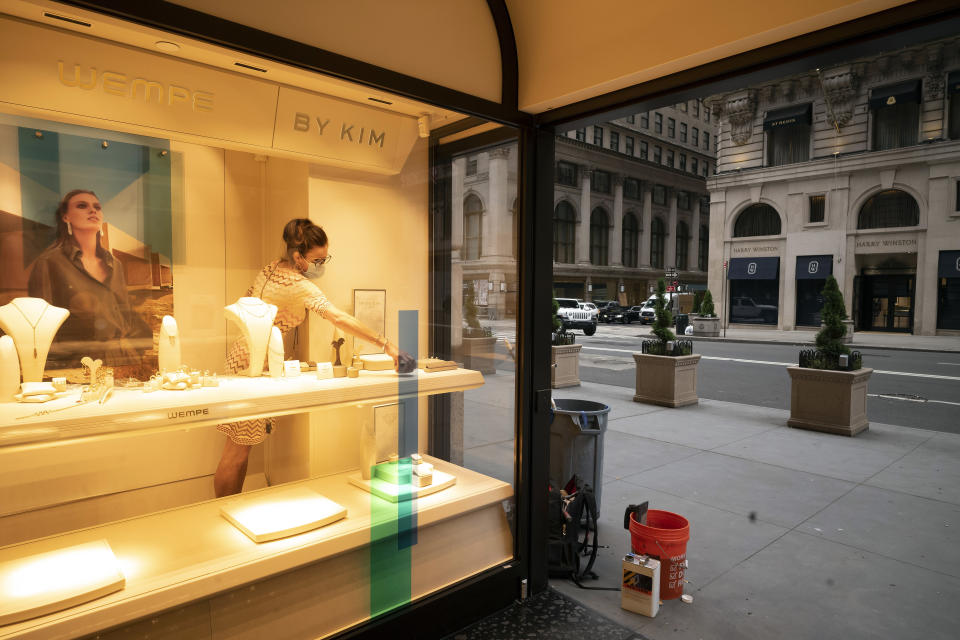 A Wempe store employee places jewellery in a store window, Thursday, June 11, 2020, in New York's Fifth Avenue shopping district. The jeweler is open for in-store and curbside pickup. In the virus times, the near-term and maybe even longer-term impact is undoubtedly going to be ugly. Job losses have been racking up, businesses facing bankruptcy, cultural institutions going under, entire industries like restaurants forced to reconsider everything they do. (AP Photo/Mark Lennihan)