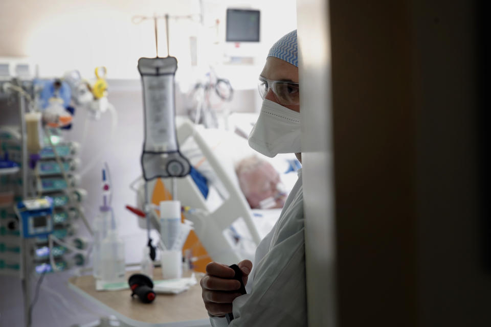 A member of the medical staff stands in a room with a patient affected by the COVID-19 virus in the ICU unit at the Charles Nicolle public hospital, Thursday, April 15, 2021 in Rouen, France. A renewed crush of COVID-19 cases is again forcing intensive care units across France to grapple with the macabre mathematics of how to make space for thousands of critically ill patients (AP Photo/Christophe Ena)