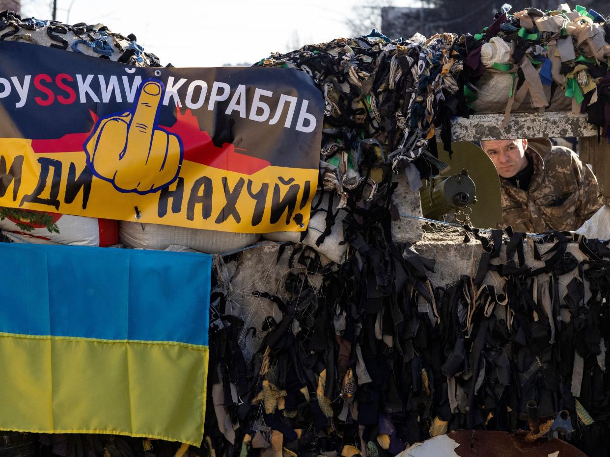 A Ukrainian serviceman stands guard next to a flag of Ukraine and a banner which reads as "A Russian ship go fuck yourself!" at a military check point in the center of Kyiv on March 15, 2022, on the 20th day of the Russian invasion of Ukraine.