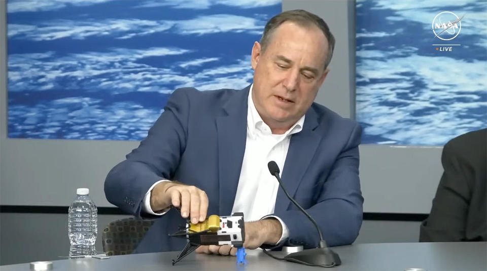 Steve Altemus, Intuitive Machines CEO and co-founder, uses a model of the company's Odysseus moon lander to illustrate how the spacecraft likely tipped over during touchdown Thursday. Based on telemetry, it appears the lander's top section may be resting on a rock (the small blue model). It's also possible the spacecraft tipped over on sloping terrain or even caught one of its foot pads in a crevice. / Credit: NASA TV