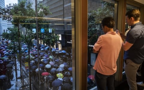 People look out from a pedestrian footbridge while demonstrators march along a road as rain falls during a protest in the Central district of Hong Kong - Credit: Justin Chin/Bloomberg