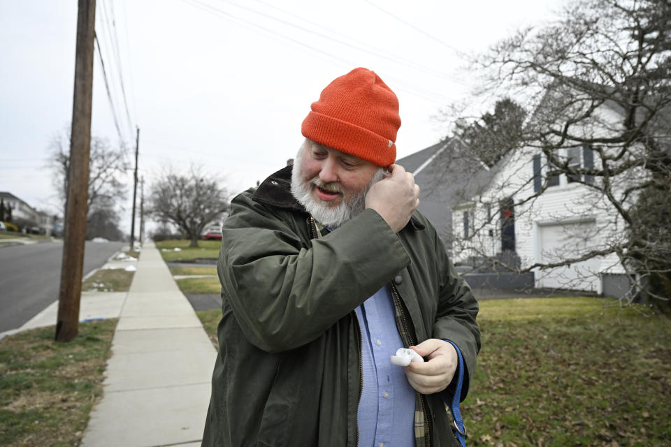 Casey Rosseau places earbuds in his ears to listen to an e-book while he walks with his dog in West Hartford, Conn., Feb. 1, 2024. Rosseau, who estimates he reads about 200 books a year, said he'd like to see more regulation of what publishers can charge libraries. Libraries have been grappling with soaring costs of digital titles, both e-books and audio books, that libraries typically lease from publishers for a year or two, with limited usage. (AP Photo/Jessica Hill)