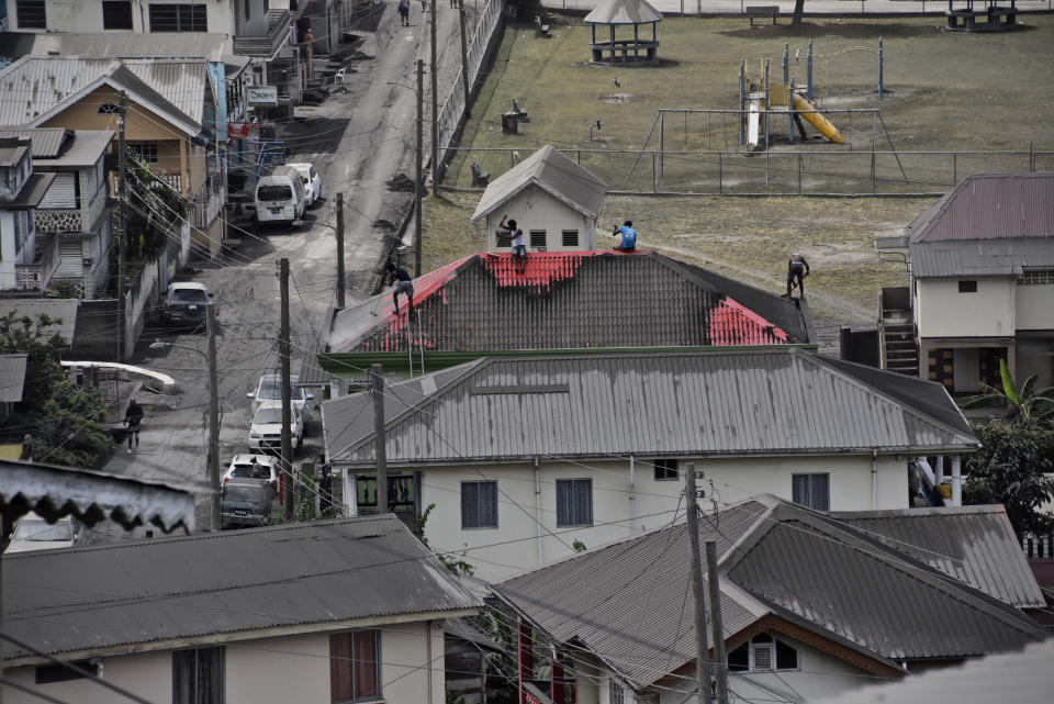 People clean volcanic ash from the red roof of a home after La Soufriere volcano erupted, in Wallilabou, on the western side of the Caribbean island of St. Vincent, Monday, April 12, 2021. La Soufriere volcano fired an enormous amount of ash and hot gas early Monday in the biggest explosive eruption yet since volcanic activity began on the eastern Caribbean island of St. Vincent late last week. (AP Photo/Orvil Samuel)