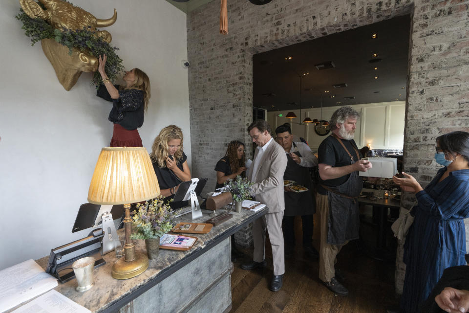 In this Saturday, June 19, 2021, photo, Caroline Styne, owner and wine director at The Lucques Group, top left, hangs a fresh floral wreath decoration to welcome customers, while her staff readies for arriving customers at the A.O.C. Brentwood restaurant in Los Angeles. Styne has turned away dozens of customers at the company's A.O.C. West Hollywood restaurant because she doesn't have the staff to serve them, leaving seats empty. (AP Photo/Damian Dovarganes)