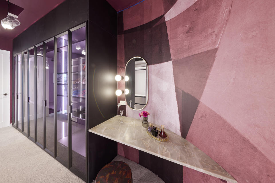 A pink textured wall with makeup mirror and black wardrobes on the left