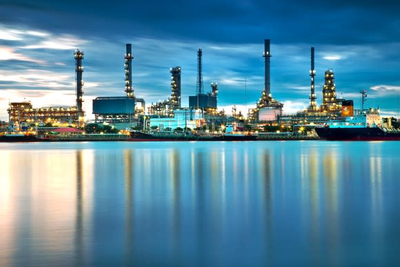 Oil refining facility on a body of water, in front of a mostly cloudy sky near dawn or dusk.