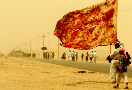 FILE PHOTO: An Iraqi Shiite man carries a flag stained with the blood of men who wounded themselves to demonstrate their love to the Imam, as he walks along with tens of thousands of religious Iraqi's on their way to the central city of Kerbala through a sand storm April 19, 2003. Thousands of Iraqi Shi'ite Muslims beat their chests with their hands and waved black and green flags in a passionate celebration of a religious pilgrimage banned for a quarter century under Saddam Hussein. Men in robes and women draped in flowing black chadors streamed along narrow lanes and through palm tree orchards from towns and villages in southern Iraq to Najaf, from where they will go on to the city of Kerbala to mark one of the holiest events in the Shi'ite calendar, on April 23. REUTERS/Yannis Behrakis/File photo