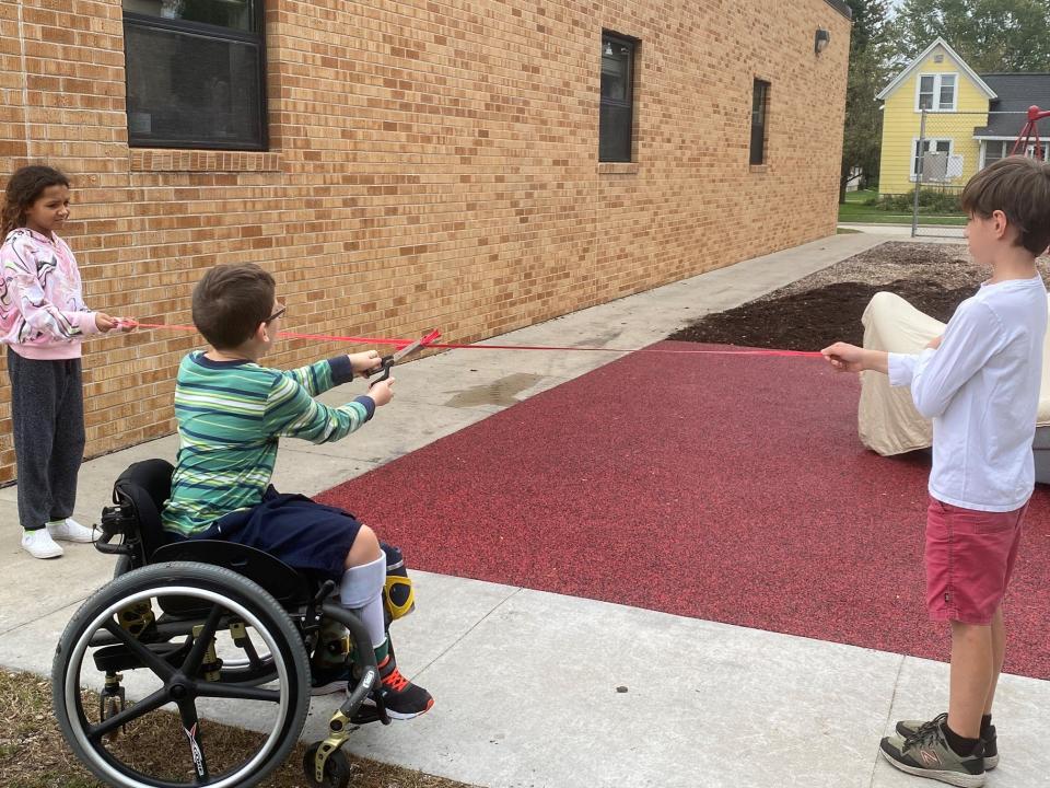 STEM Academy fourth grader Owen Wild cuts the ribbon revealing the school's new accessible playground turf and equipment. Holding the ribbon are Amerakiss Cary and Carter Bruno.