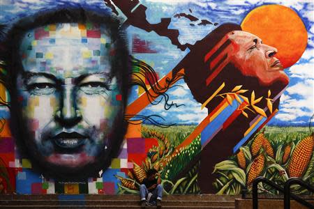 A man sits next to a mural depecting the late Venezuelan President Hugo Chavez in downtown Caracas September 23, 2013. REUTERS/Jorge Silva