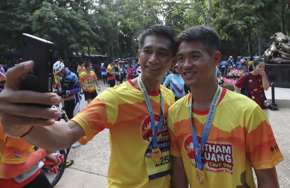 A runner takes a selfie with former soccer coach Ekkapol Chanthawong, right, who was rescued from a flooded cave, after a marathon and biking event in Mae Sai, Chiang Rai province, Thailand, Sunday, June 23, 2019. Some of the 12 young Thai soccer players and their coach have marked the anniversary of their ordeal that saw them trapped in a flooded cave for two weeks with a commemorative marathon in northern Thailand. (AP Photo/Sakchai Lalit)