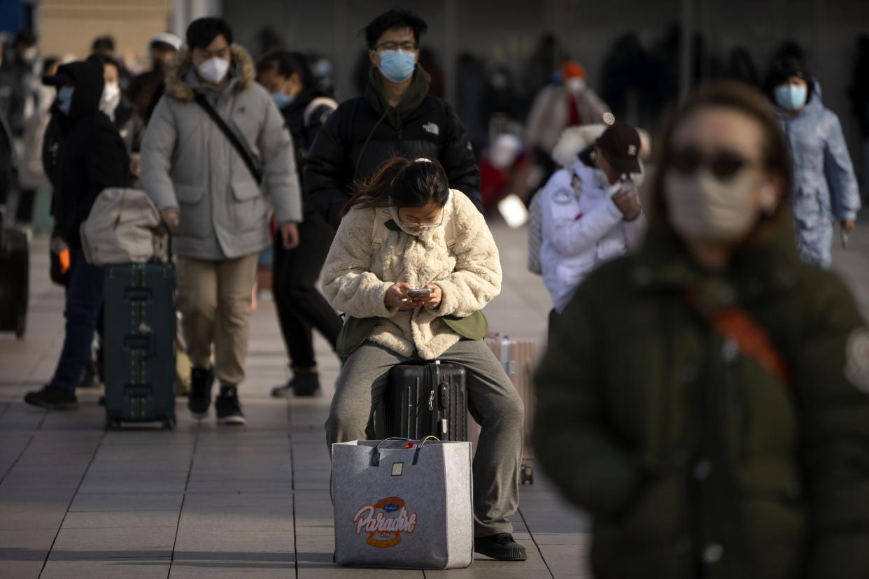 A traveler sits on her suitcase outside the entrance of the Beijing Railway Station in Beijing, Saturday, Jan. 14, 2023. Millions of Chinese are expected to travel during the Lunar New Year holiday period this year. (AP Photo/Mark Schiefelbein)