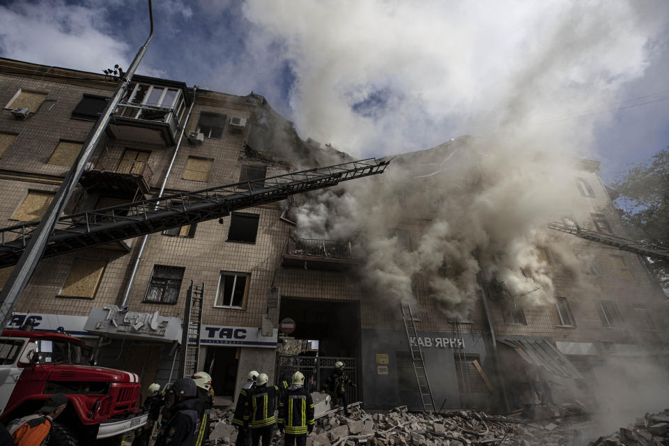 Smoke rises as a half dozen firefighters stand near a fire truck amid the rubble of a damaged building.