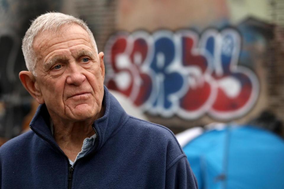 A man stands in front of a tent and a wall with graffiti on it.