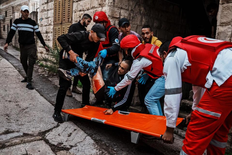 Local youth and paramedics help hoist a man onto a stretcher after he was shot twice by Israeli soldiers.