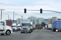 Downtown Oakland buildings are shown behind trucks lined up at the Port of Oakland in Oakland, Calif., Thursday, Feb. 18, 2021. Disadvantaged communities in America are disproportionately affected by pollution from industry or waste disposal, but their complaints have few outlets and often reach a dead end. (AP Photo/Jeff Chiu)
