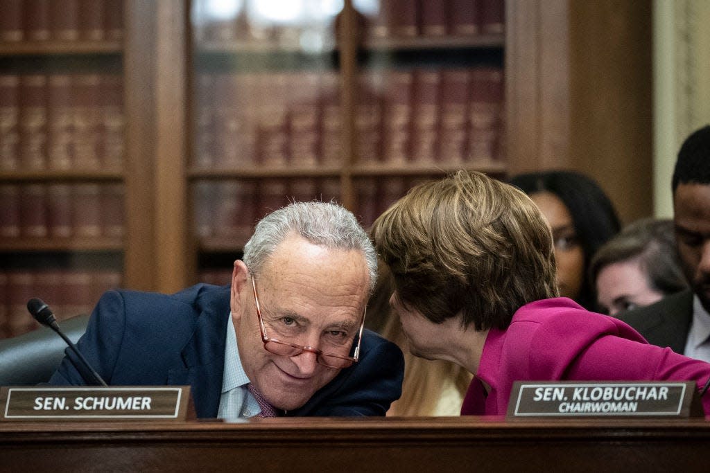 Chuck schumer smiles whiles amy klobuchar whispers into his ear