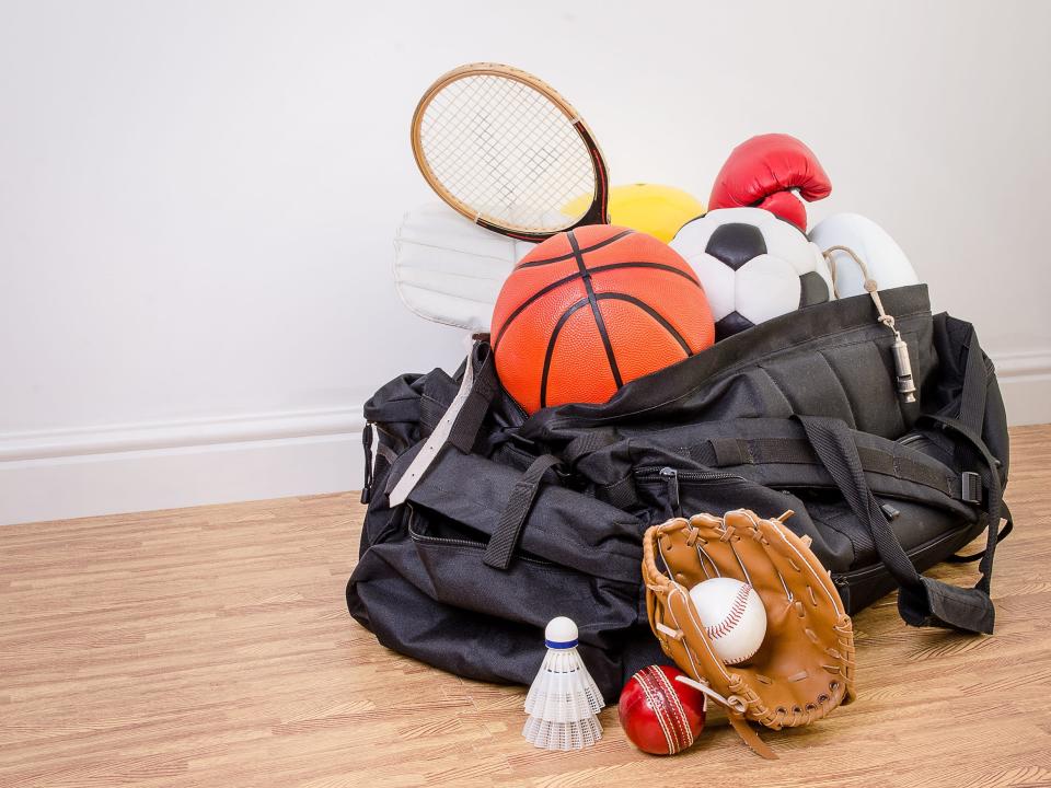 A duffle bag filled with different balls and rackets.