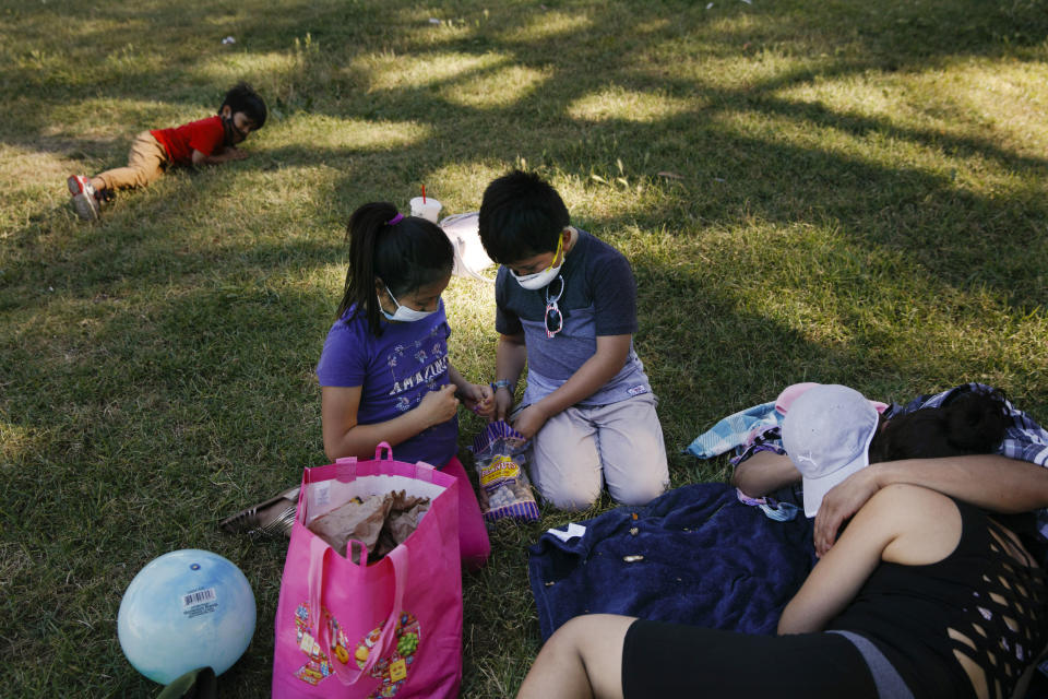 Regina Cel, left, and brother Leandro shell peanuts with their masks on next to their parents at a park during the coronavirus pandemic, in the Westlake neighborhood of Los Angeles, Thursday, May 21, 2020. While most of California is welcoming a slight return toward normal this holiday weekend, Los Angeles will not be joining the party. The nation's largest county is not planning to reopen more widely until the next summer holiday, July 4th, because of a disproportionately large share of the state's coronavirus cases and deaths that have hampered the county's ability to rebound and meet strict criteria to get more people back to work. (AP Photo/Jae C. Hong)