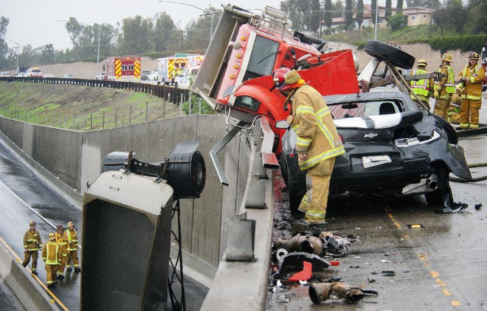 A fire captain looks at crews below keeping an eye on the trailer on the westbound 91 freeway FasTrak Express lane after the driver of a two-trailer dirt-hauling dump truck slid, tipped and wound up partially dangling off the ramp from the eastbound 91 freeway to the northbound 55 Friday, Dec. 16, 2016, in Anaheim, Calif. A late fall storm has drenched California, causing some mud flows, roadway flooding and traffic snarls as it takes parting shots at the south end of the state. (Ken Steinhardt/The Orange County Register via AP)